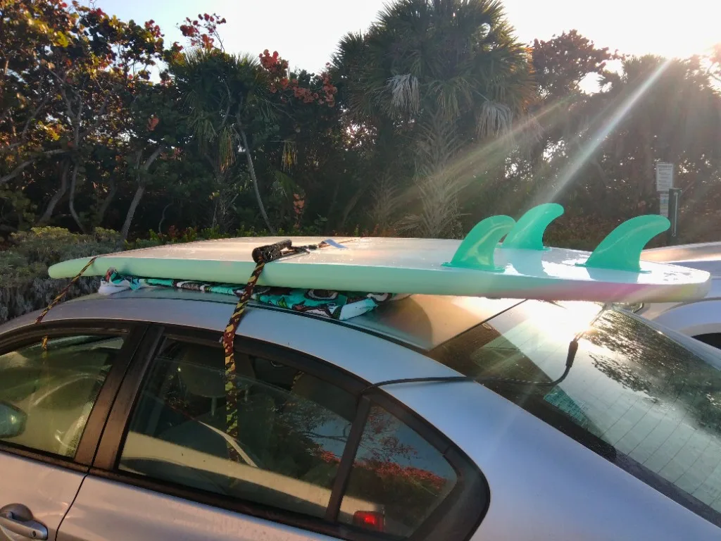 Surfboard strapped to the roof of a car at sunset